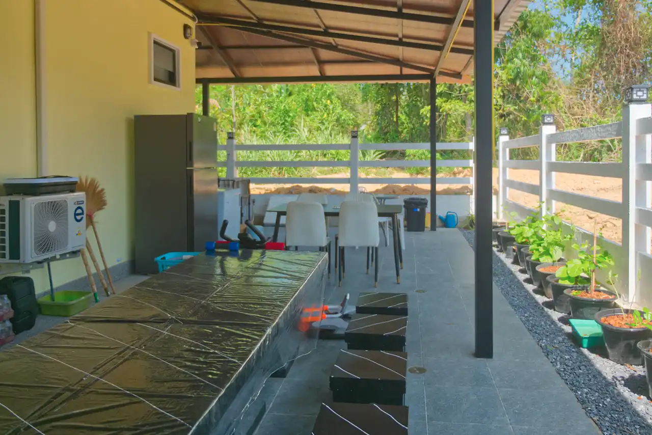 Covered outdoor terrace at Baan Bahng Can Do Krabi homestay with dining table, fridge, herb garden planters, and views over surrounding greenery