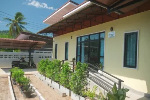 Street-facing exterior of Baan Bahng Can Do homestay in Nong Thale, Krabi, with covered carport, garden planters, and entrance ramp