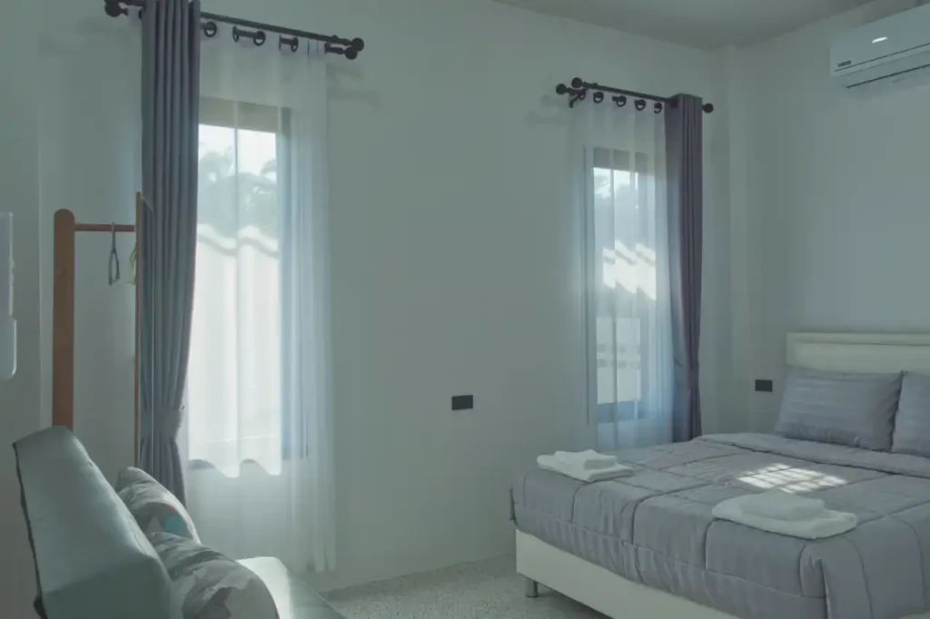Queen bedroom at Baan Bahng Can Do Krabi homestay with double bed, sofa bed, two windows with grey curtains, air conditioning, and fresh towels