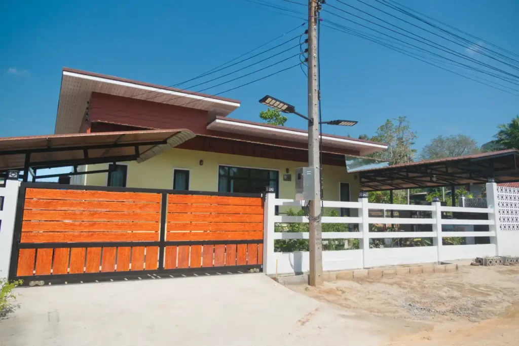 Gated entrance and exterior of Baan Bahng Can Do homestay in Nong Thale, Krabi, with timber-panel sliding gate, white perimeter fence, and covered carport