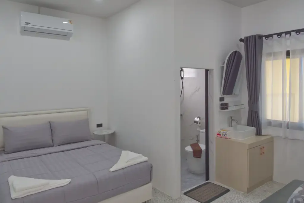Bedroom 2 at Baan Bahng Can Do Krabi homestay with queen bed, air conditioning, en-suite WC visible through open door, vanity unit, arched mirror, and garden window