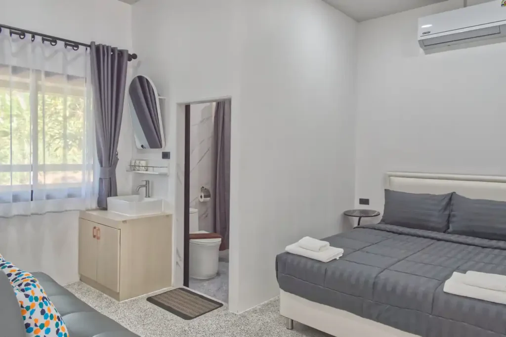Bedroom 4 at Baan Bahng Can Do Krabi homestay with queen bed, air conditioning, en-suite WC visible, vanity unit with vessel sink, arched mirror, and garden window