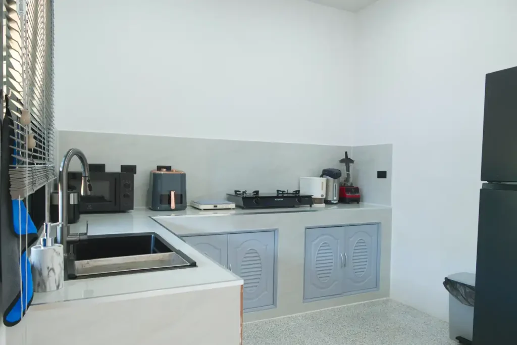 Indoor guest kitchen at Baan Bahng Can Do Krabi homestay showing full counter run with sink, microwave, toaster, gas hob, kettle, blender, and under-counter storage cabinets