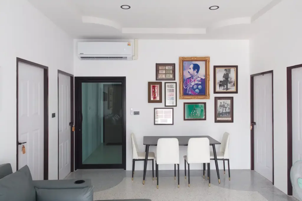 Shared dining area at Baan Bahng Can Do Krabi homestay with 4-seat dining table, air conditioning, and gallery wall of Thai royal portrait and vintage framed prints
